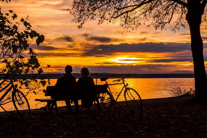 Couple on bench with bicycles watching sunset over lake