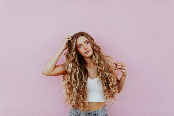 Woman with long blonde curly hair in front of pink wall