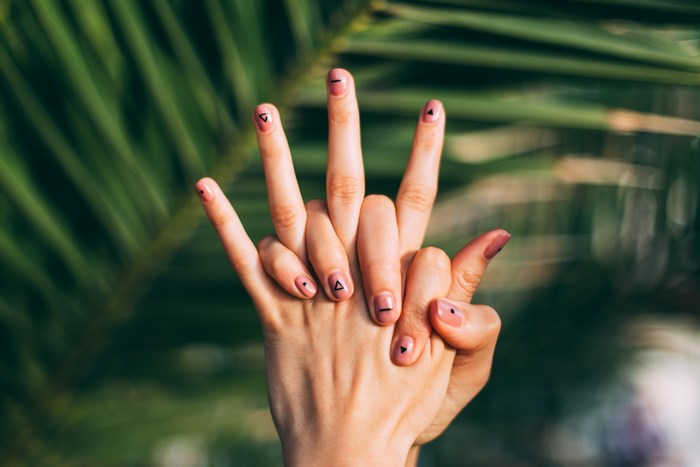 Hands with geometric nail art against palm leaves