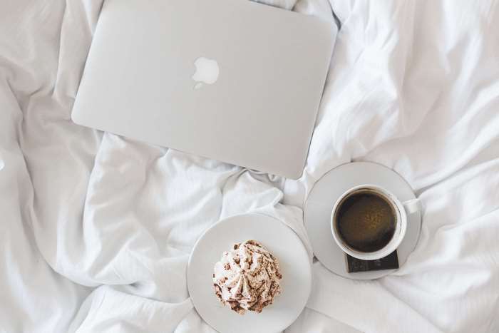 Apple MacBook with Coffee and Cake on White Bed