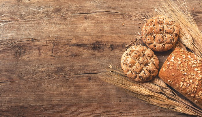 Bread rolls and loaf with wheat on wooden board