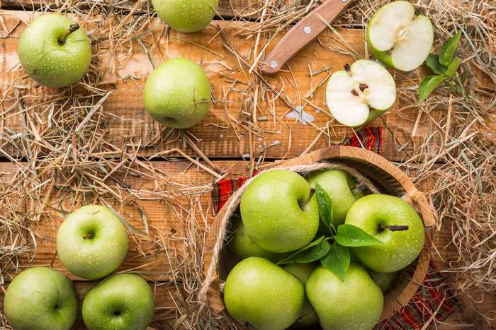 Green apples in a basket with hay and a knife