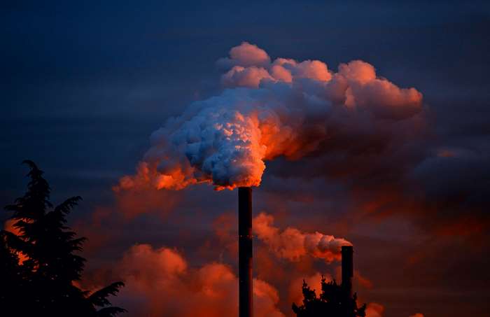 Factory chimney emitting smoke at sunset