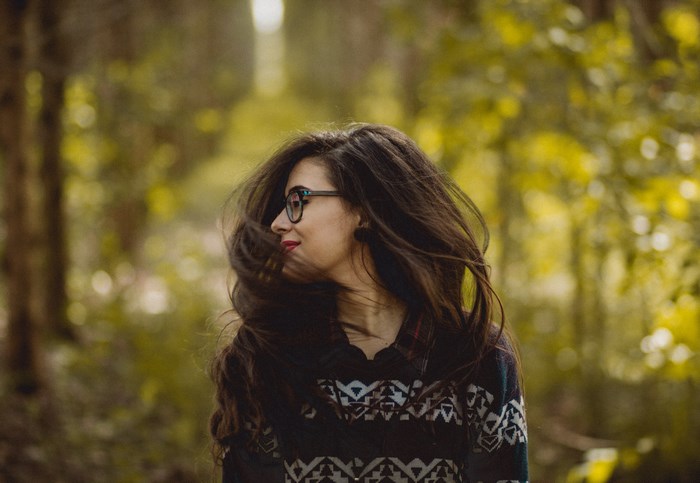 Woman with long brown hair wearing glasses and a sweater in a forest