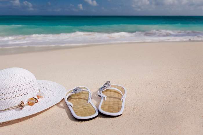Beach scene with hat and flip flops on sand