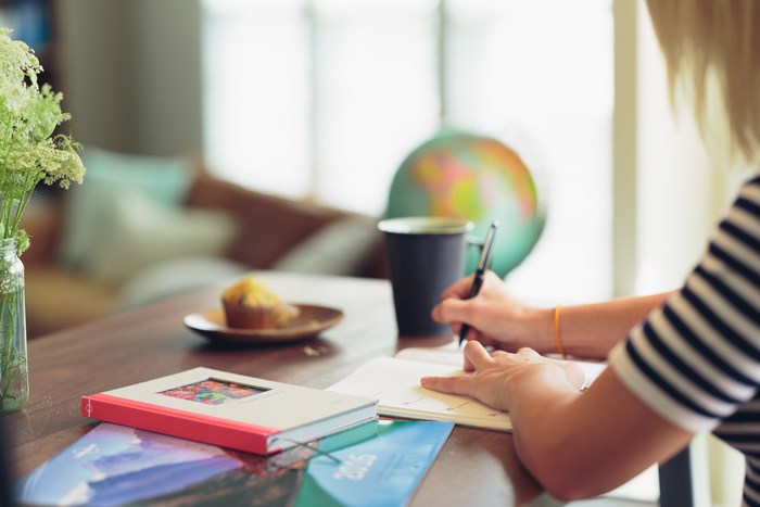 Woman writing in a journal at a table with a muffin and globe