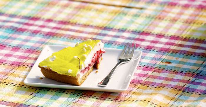 Slice of yellow frosted pastry with red filling on a plate with a fork