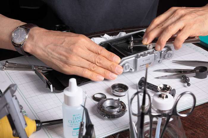 Hands repairing a vintage Nikon camera with tools