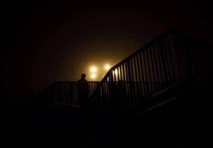 Silhouettes of people on a bridge at night with street lights