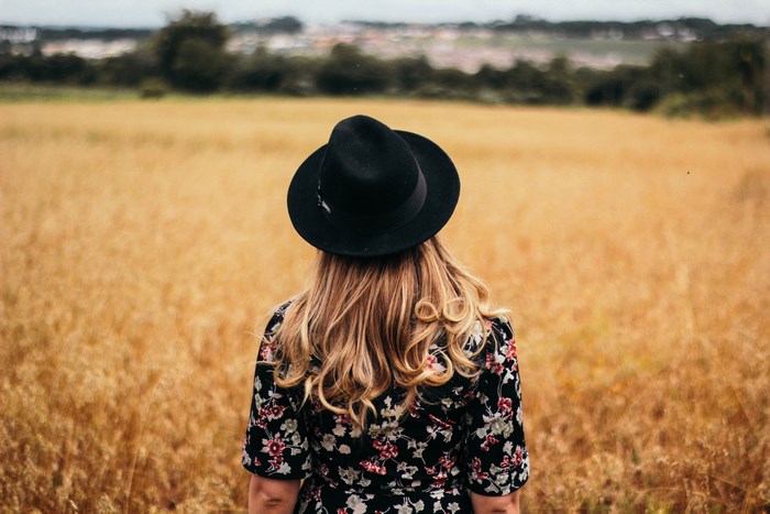 Woman with blonde curly hair wearing a black hat in a field