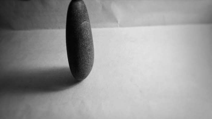 A single dark stone standing on a white surface with shadow