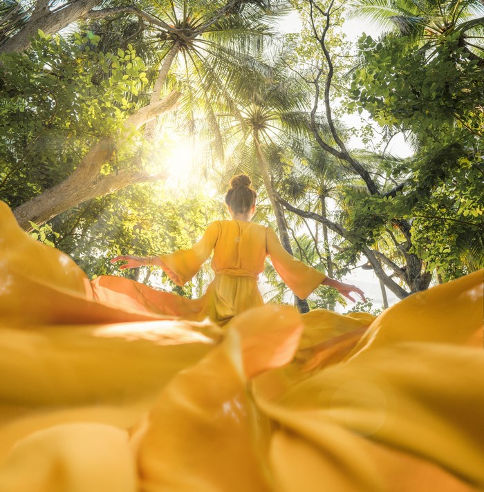Woman in yellow dress under palm trees with sunlight