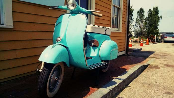 Vintage turquoise Vespa scooter parked by a wooden building