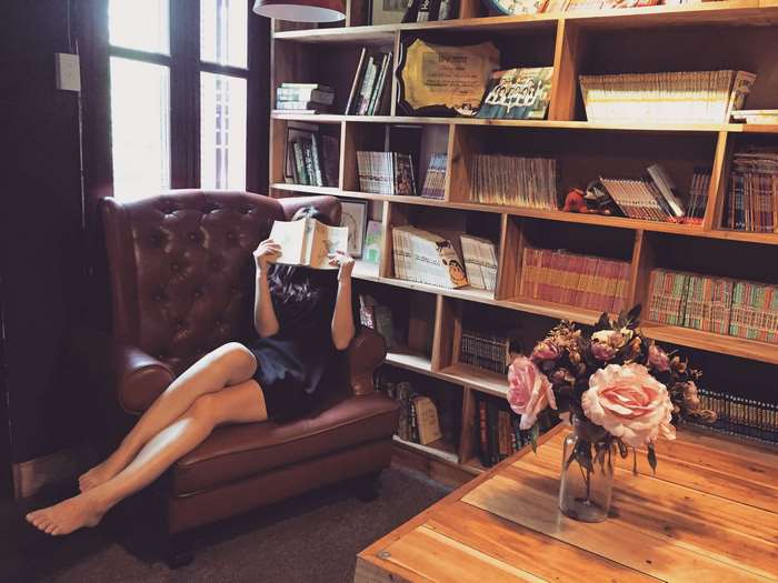 Woman Reading Book on Leather Couch in Cozy Library