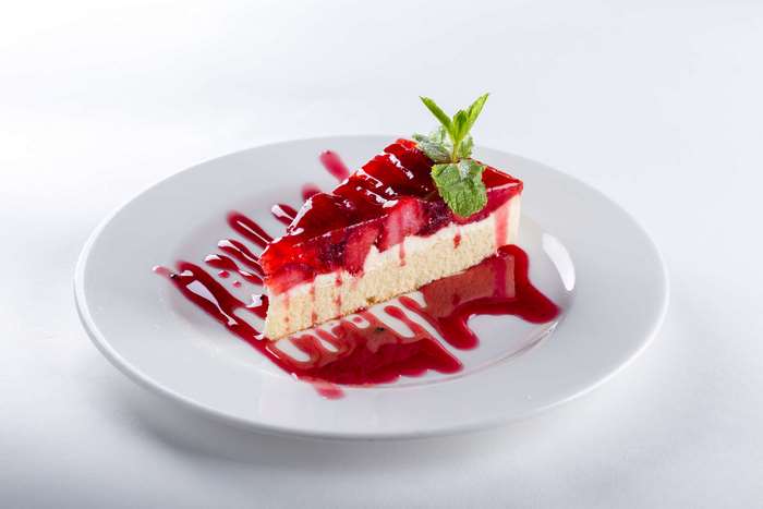 Slice of strawberry cheesecake with red sauce and mint