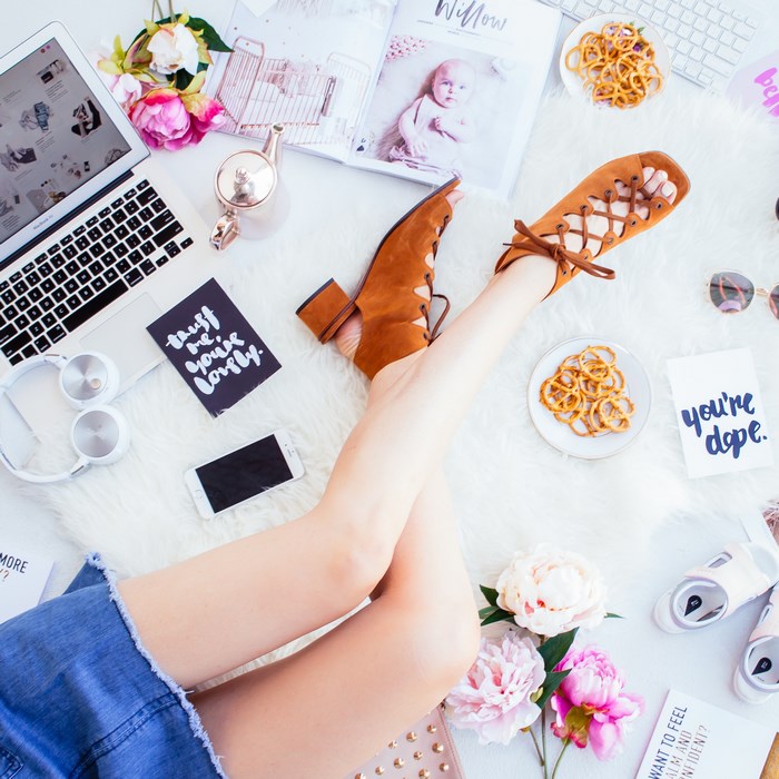 Flat lay of a woman's legs with laptop, shoes, and snacks