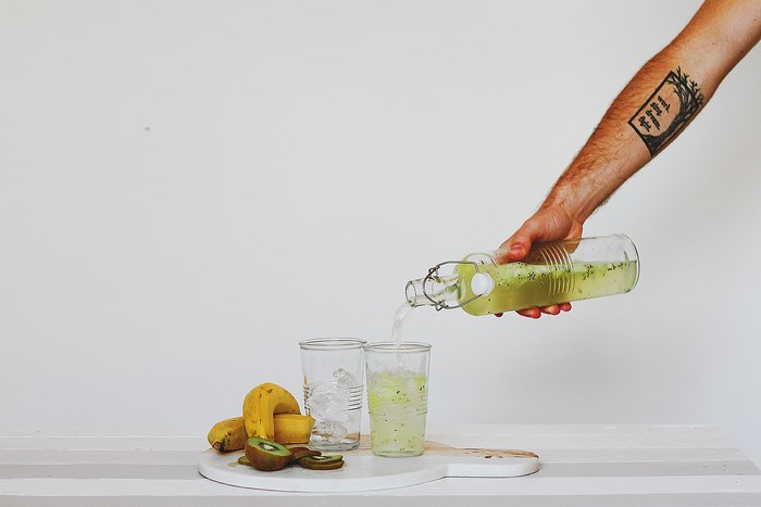 Man pouring kiwi drink into glass with banana and ice