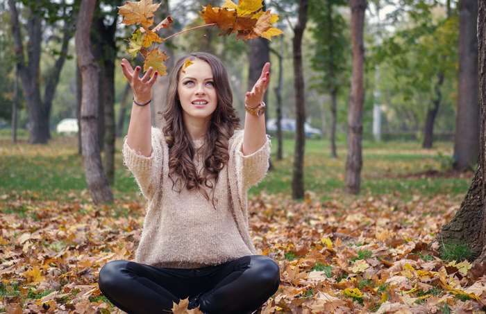 Young woman throwing leaves in a park during autumn
