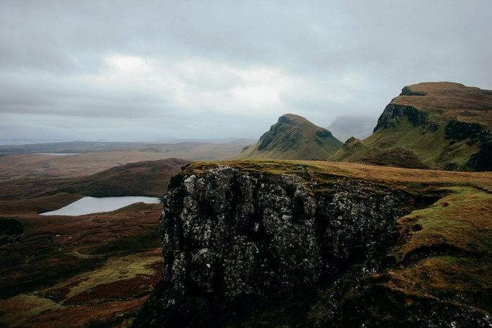 Rocky cliff overlooking a vast Scottish landscape with hills and a lake