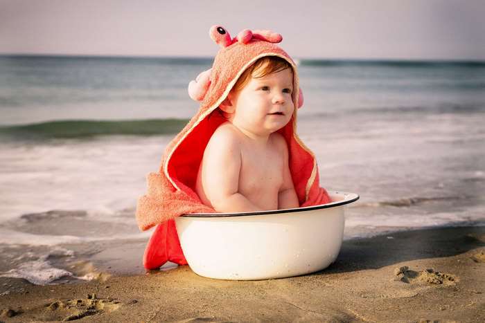 Baby in crab towel sitting in a wash pot on the beach