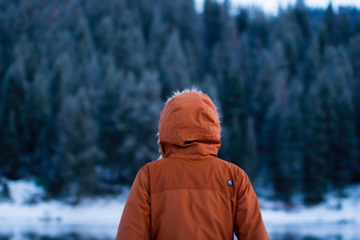 Person in orange winter jacket looking at forest