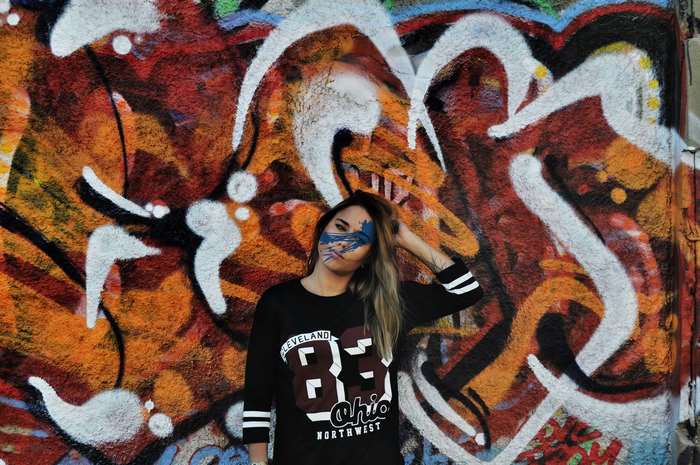 Woman with face paint in front of graffiti wall