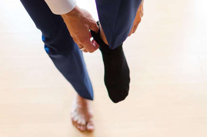 Man putting on black sock with navy pants