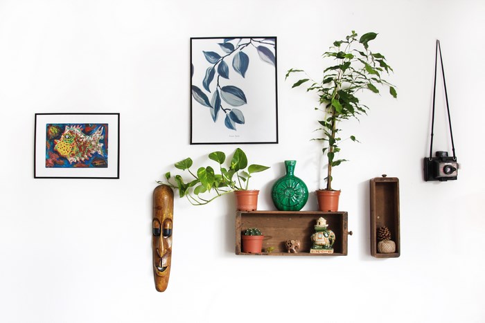 Wall decoration with paintings, plants, and a wooden mask