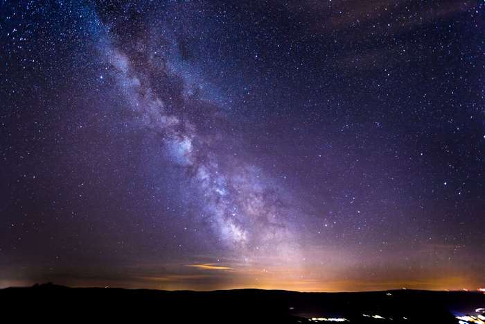 Milky Way over a dark landscape with distant city lights