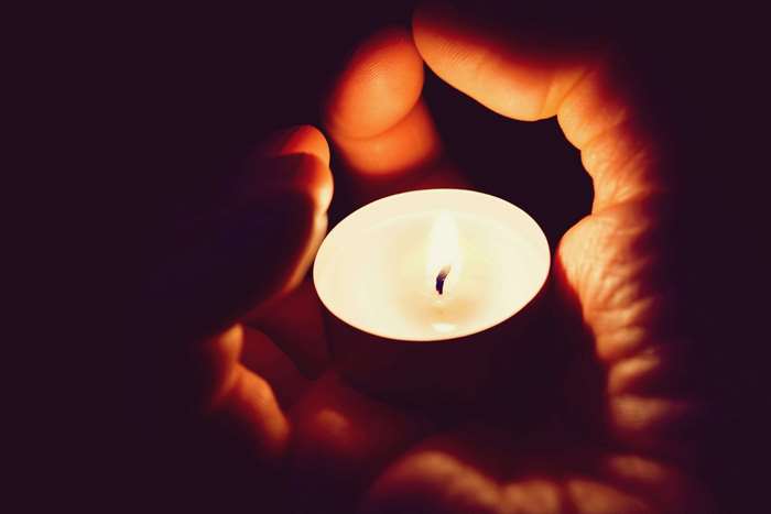 Hands holding a lit candle in the dark