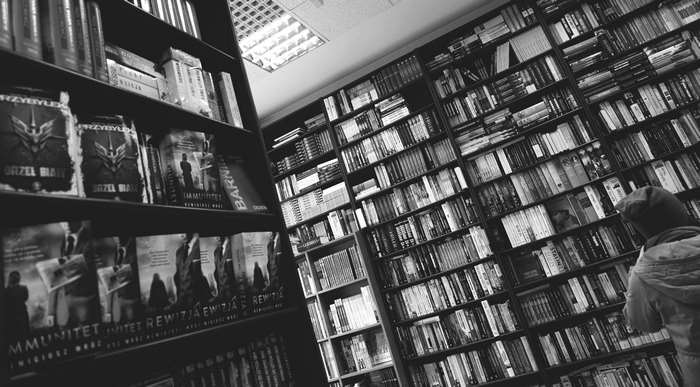 Black and white image of a bookstore with shelves full of books and a person browsing