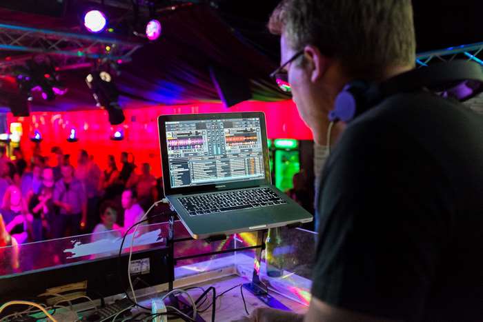 DJ with headphones playing music on laptop in nightclub