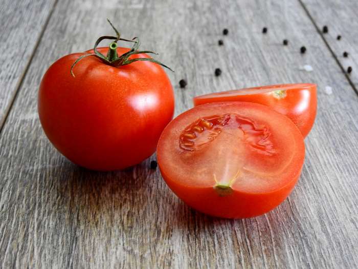 Whole and halved tomatoes with peppercorns on wooden table