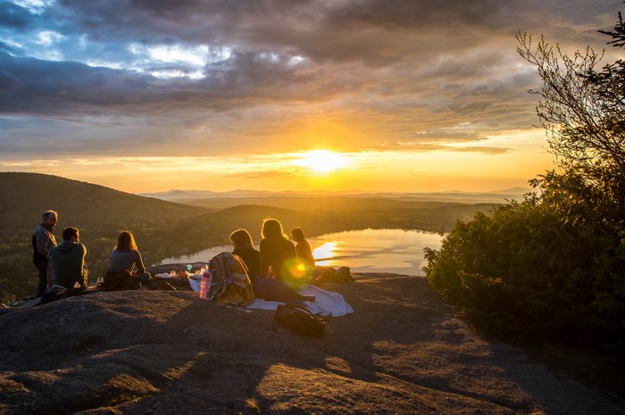 Group of friends enjoying a sunset picnic on a rocky hilltop overlooking a lake