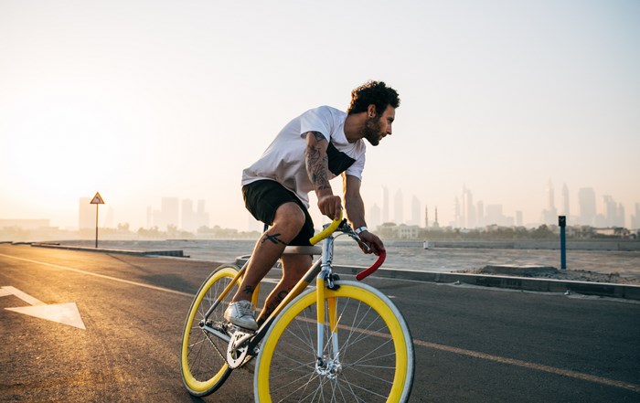 Man riding a yellow fixie bike at sunrise with cityscape