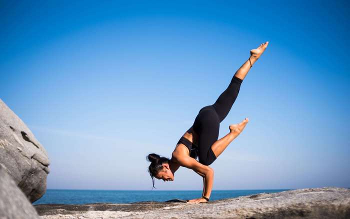 Woman performing yoga handstand on rocks by the ocean 4K