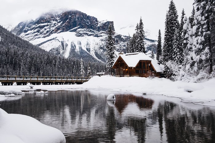 Wooden cabin by a snowy lake with mountains