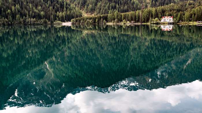 House by a forest lake with mountain reflections