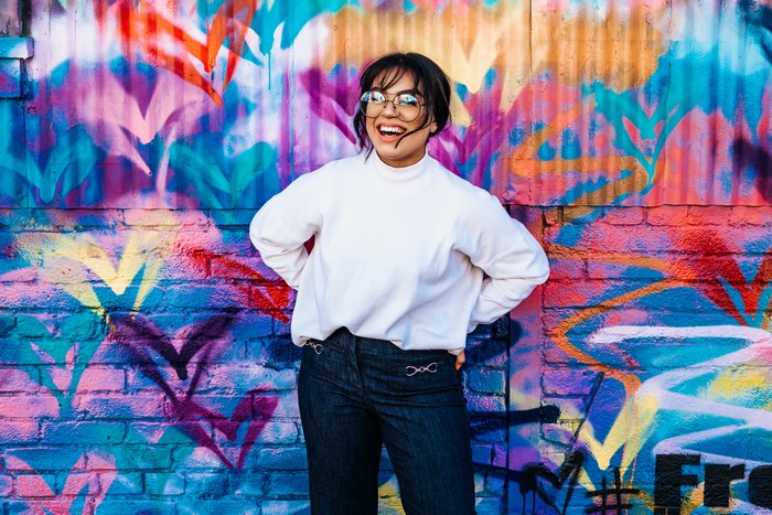 Woman in white sweater and jeans posing against graffiti wall