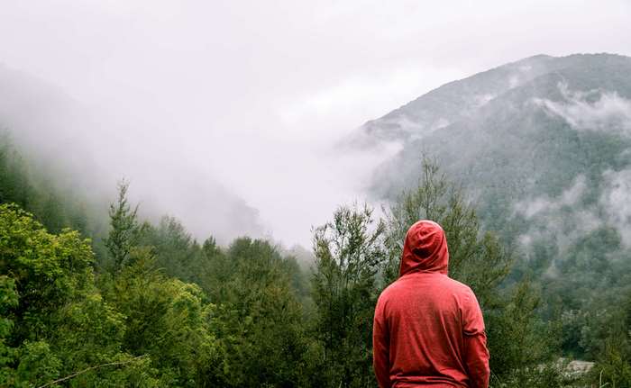 Man in red hoodie looking at foggy mountains and forest