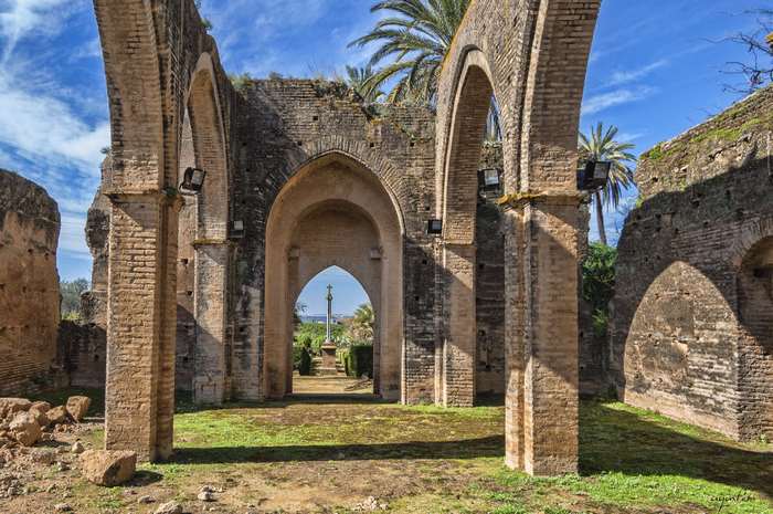 Ruins of Castilleja de Talhara with arches and palm trees