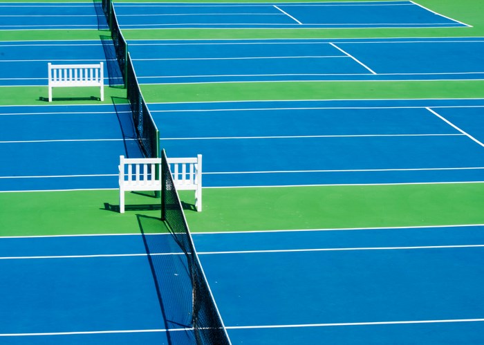 Blue and green tennis courts with white benches and nets