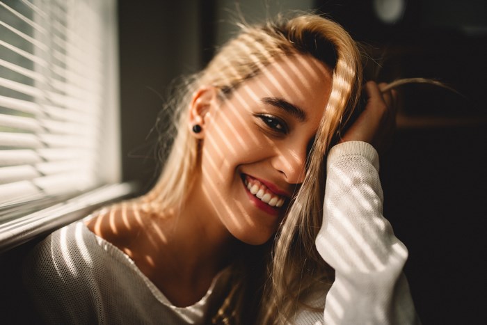 Woman with blonde hair smiling near window blinds