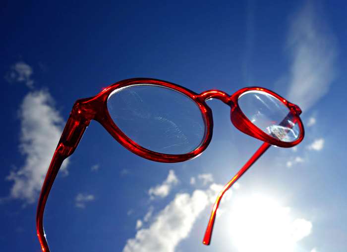 Red Eyewear Against Blue Sky with Clouds and Sunlight