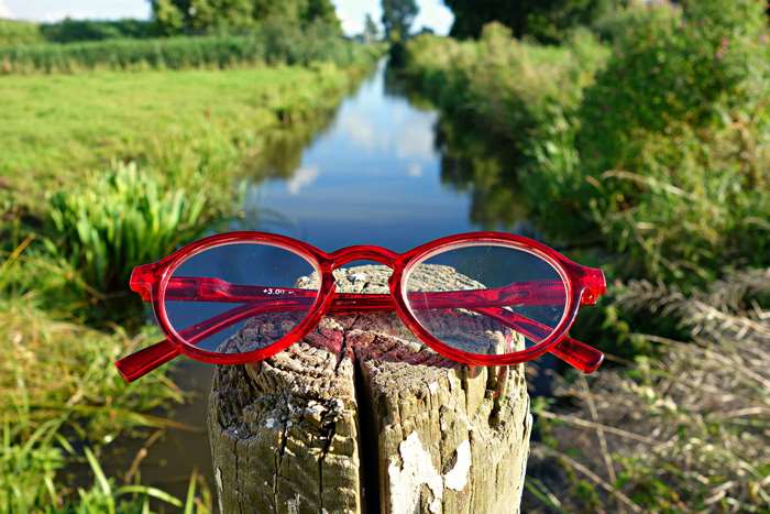 Red reading glasses on a wooden post near a canal