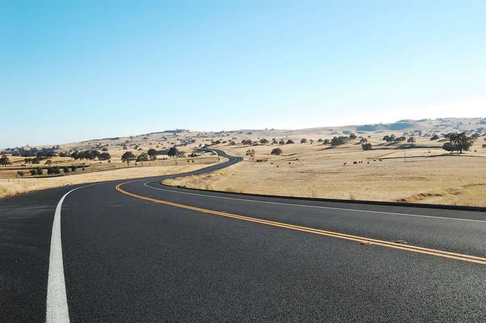 Winding road through a dry, hilly landscape with scattered trees