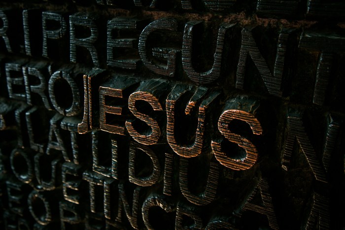 Close-up of carved letters spelling "JESUS" on a dark surface