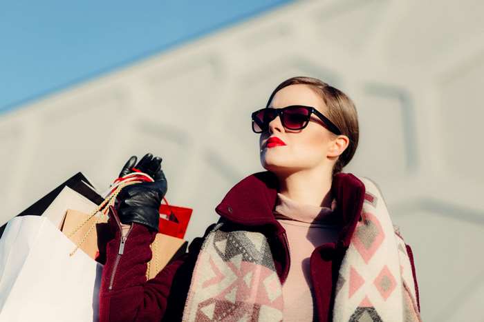 Woman in sunglasses and coat holding shopping bags
