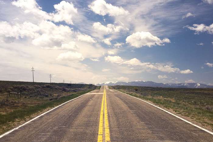 Endless highway stretching towards snow-capped mountains under a cloudy sky