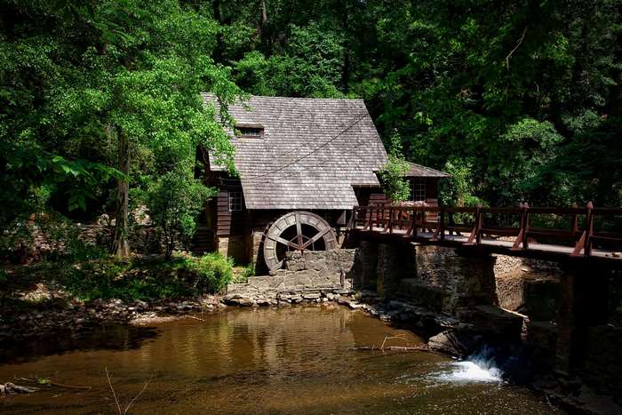 Old wooden mill with water wheel and bridge in forest